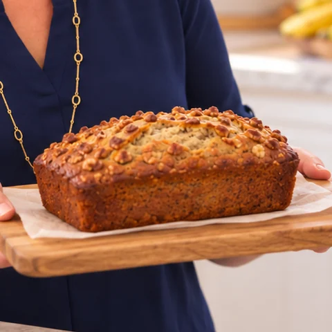 Laura holding a freshly baked loaf of banana bread topped with toasted nuts.